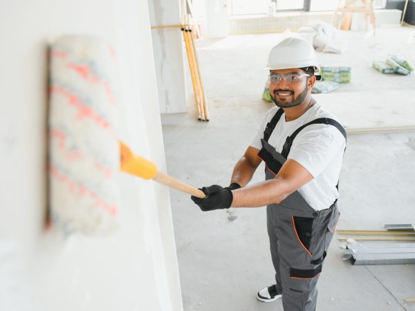 An Indian apartment repair worker paints a white wall with a roller.