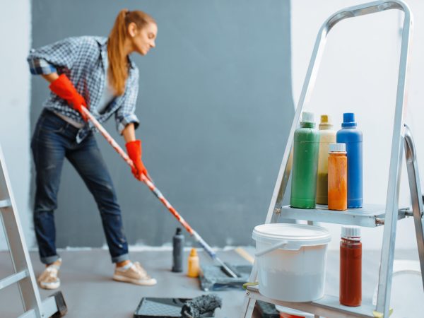 Female house painter paints walls indoor. Home repair, laughing woman doing appartment renovation, room decoration renovating