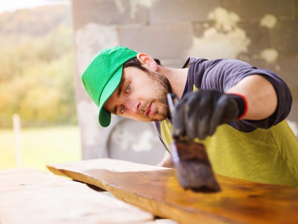 Handyman varnishing pine wooden planks in patio outside the new house
