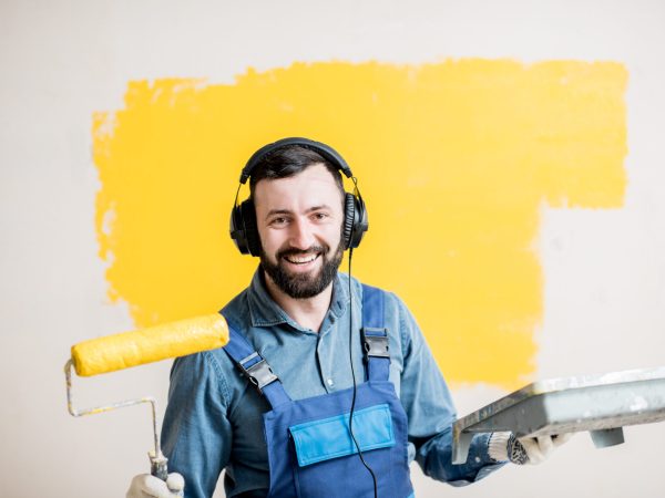 Portrait of a happy repairman listening to the music with headphones during the painting process indoors