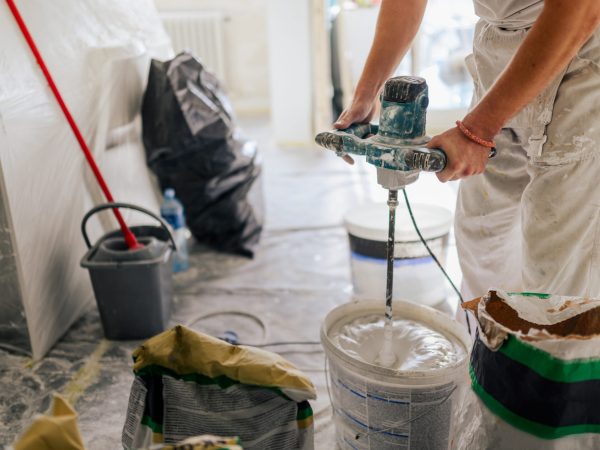 Close up of constructor's hands using manual cement mixer and making plastering material for plastering and skim coating walls. Cropped picture of worker using mixer in a house in renovation process.